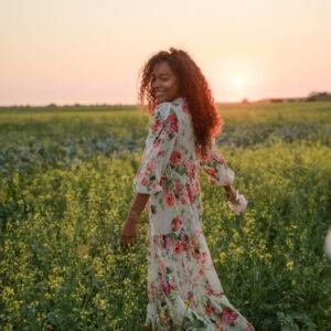 Cheerful woman in floral summer dress dancing in flowery meadow at sunset
